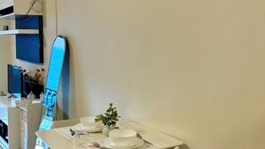 A modern dining area with a white table set for two, wooden chairs, and a small plant centerpiece.