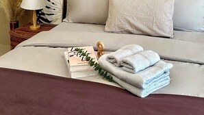 A neatly made bed with a decorative wall piece, a bedside lamp, and a stack of towels.