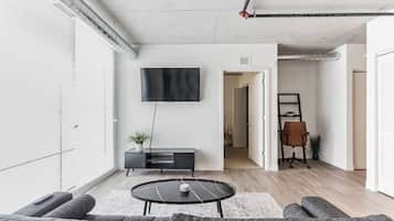 A modern living room with a flat-screen TV mounted on the wall, a black console table with a plant, a round coffee table, and a gray sofa.
