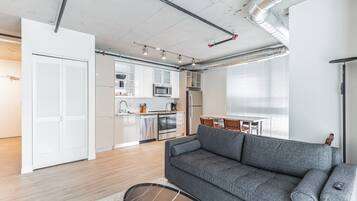 A modern apartment with a grey sofa, a kitchen with white cabinets, and a dining area.