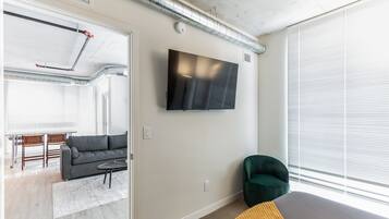 A modern living room with a grey sofa, a green armchair, and a flat-screen TV mounted on the wall.