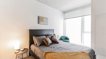 A modern bedroom with a bed, bedside lamp, and a window with blinds.