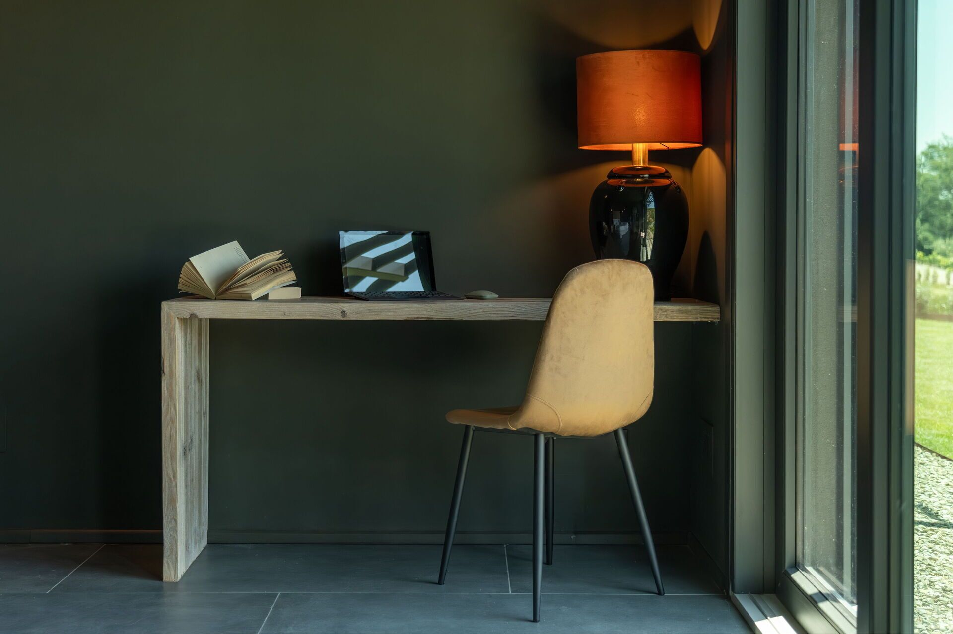 Un espace de travail comprenant un bureau en bois, une chaise, un ordinateur portable, des livres et une lampe.