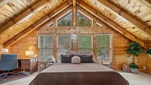 A cozy attic bedroom with a large bed, wooden walls, and a sloped ceiling. - Round Top Way Cabin by Beyond Expectations: 6BR Luxury Cabin w/ Hot Tub & Sauna (Sevierville)