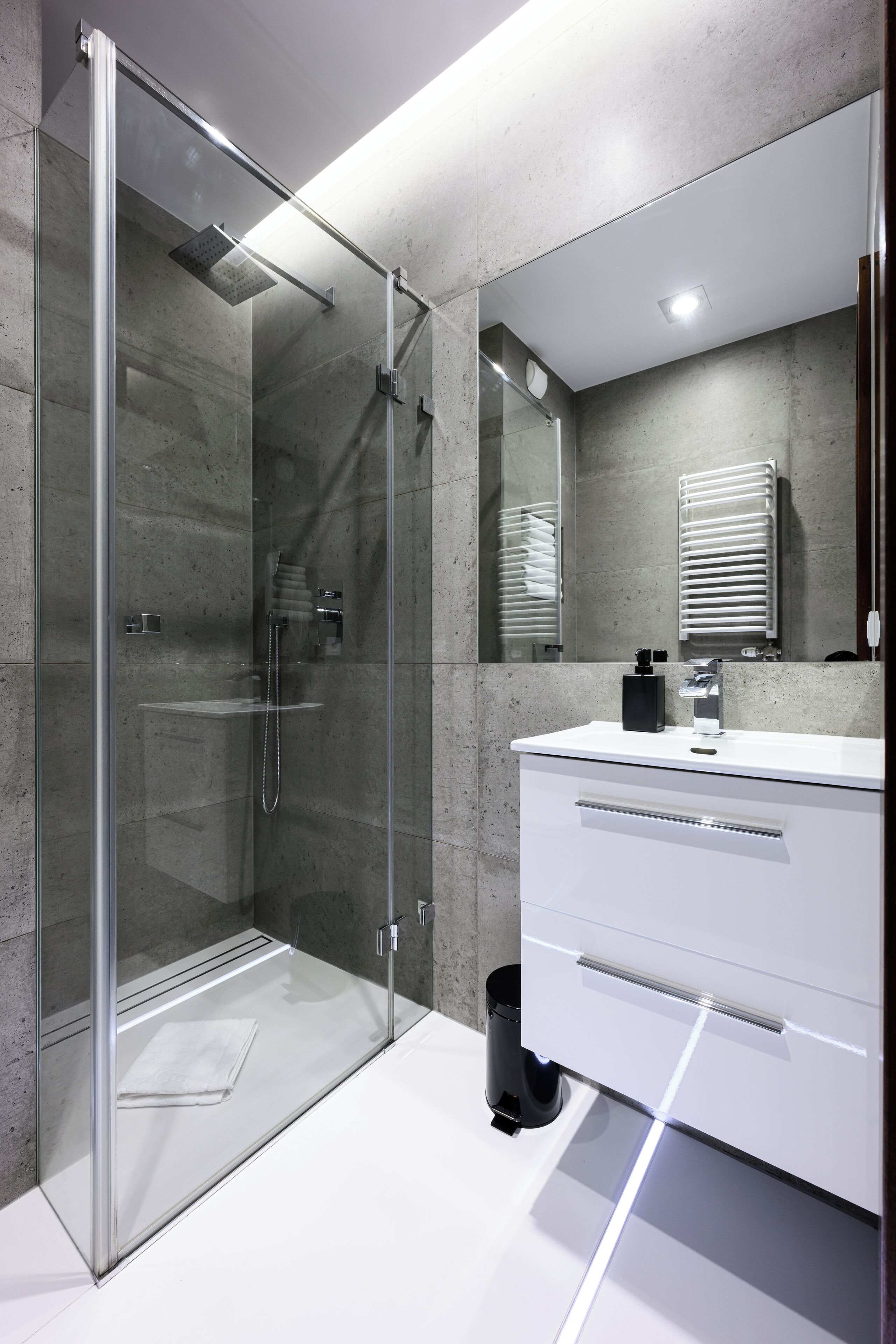 A modern bathroom with a glass-enclosed shower, a white vanity with a mirror, and a towel rack.