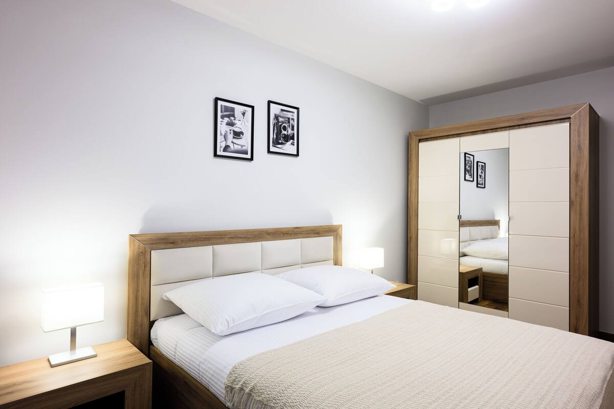 A neatly arranged bedroom with a bed, bedside tables, a wardrobe, and two framed pictures on the wall.