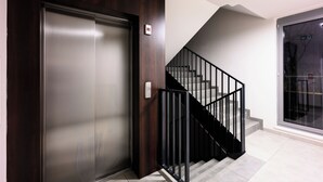 A modern elevator with a metallic finish, a wooden panel design, and a black metal staircase with a handrail. - Native Apartments Masarska 8 (Kraków)