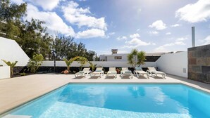 Una piscina con sillas de descanso, rodeada por un edificio blanco de fachada de piedra, y árboles al fondo.