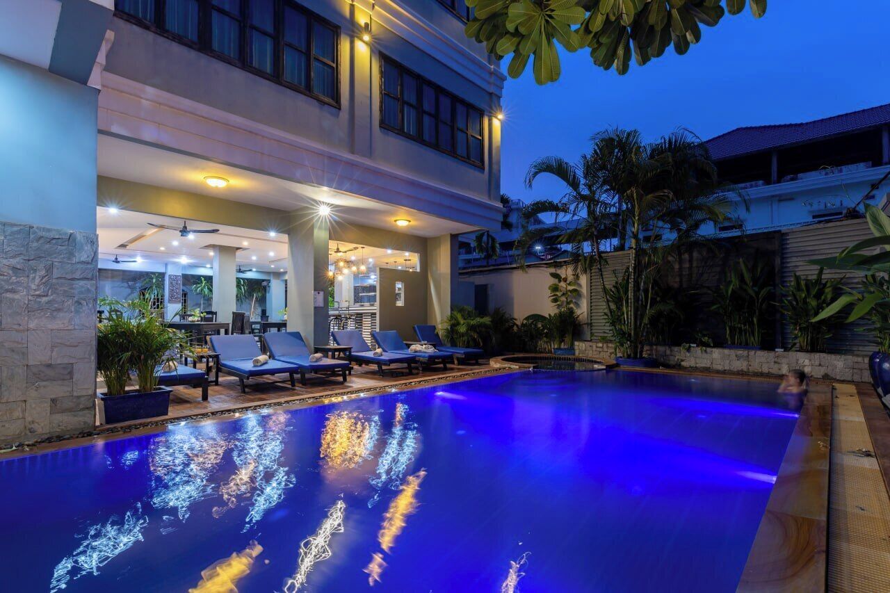 A swimming pool with blue lighting, lounge chairs, and a restaurant area with tables and chairs.