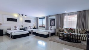 A modern hotel room with two beds, a sofa, a coffee table, and a view of the city.