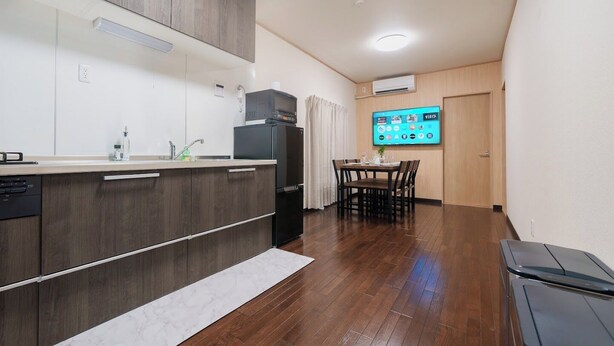 A compact kitchen with a built-in microwave, a refrigerator, and a dining area with a table and chairs. - Daiyamondo Yui Ooyamaten (Tokyo)