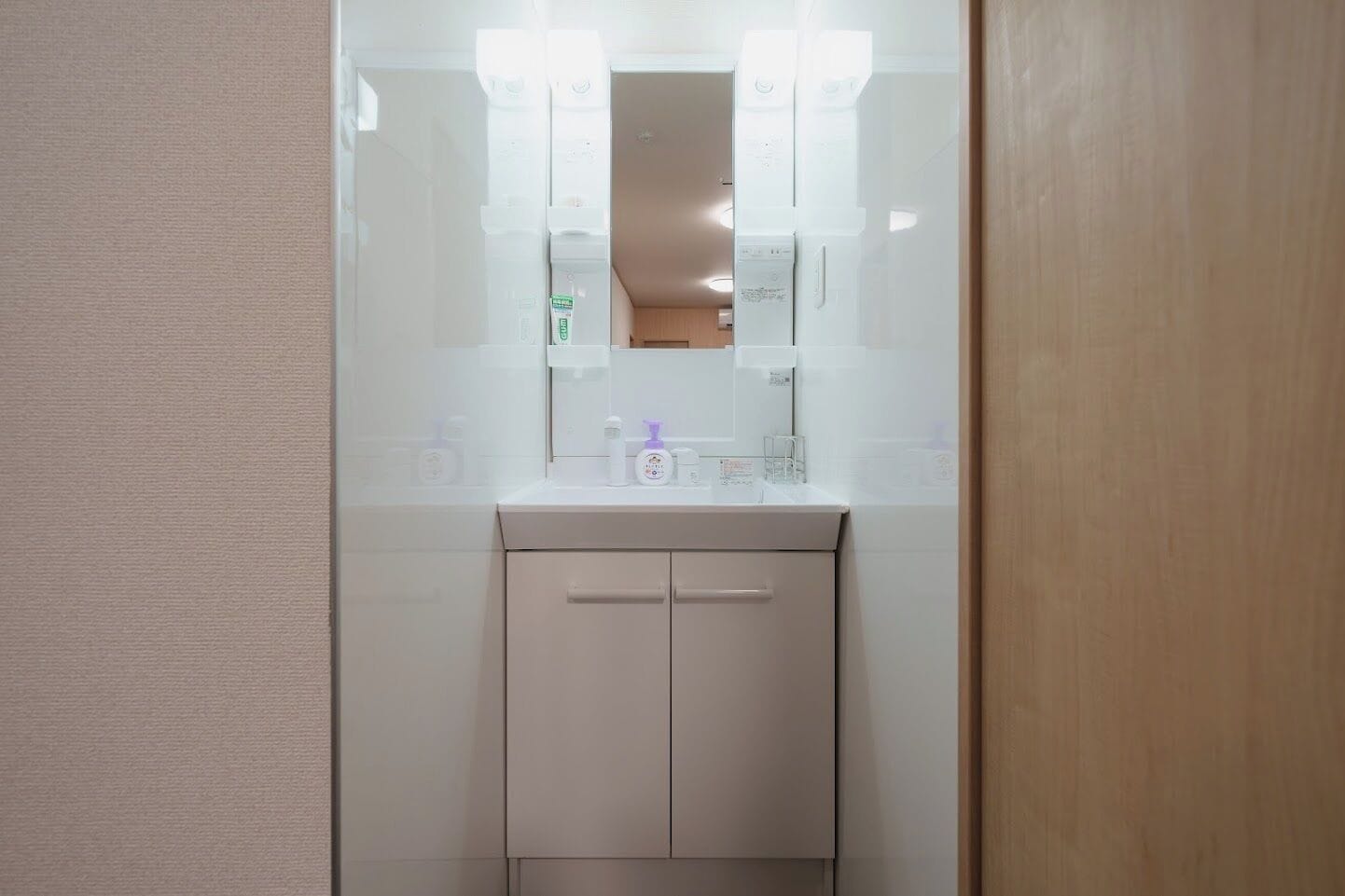 Un baño pequeño con un lavamanos blanco, dos luces en el techo y un espejo sobre el lavamanos.