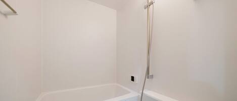 A modern bathroom with a white bathtub, a handheld showerhead, and a wall-mounted control panel.