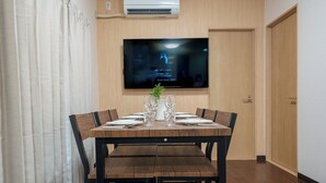 A dining area with a wooden table set for four, a flat-screen TV mounted on the wall, and a door to the right. - Daiyamondo Yui Ooyamaten (Tokyo)