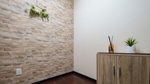 A room with a stone-patterned wall, a wooden cabinet, and a potted plant. - Daiyamondo Yui Ooyamaten (Tokyo)