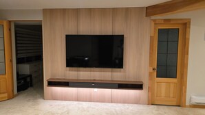 Una stanza con una grande TV a schermo piatto fissata a una parete di legno, uno scaffale integrato sottostante e una porta con un pannello in vetro satinato.