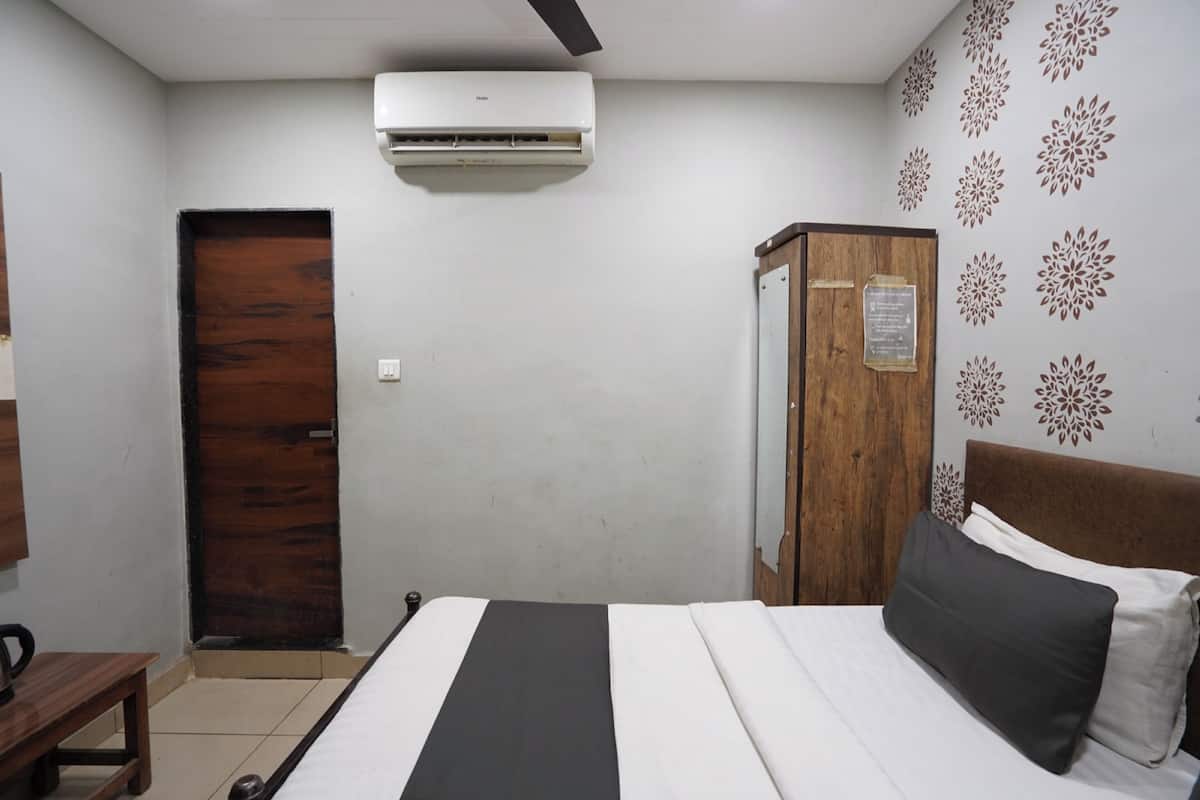 A bedroom with a bed, a wooden wardrobe, a door, and an air conditioning unit.