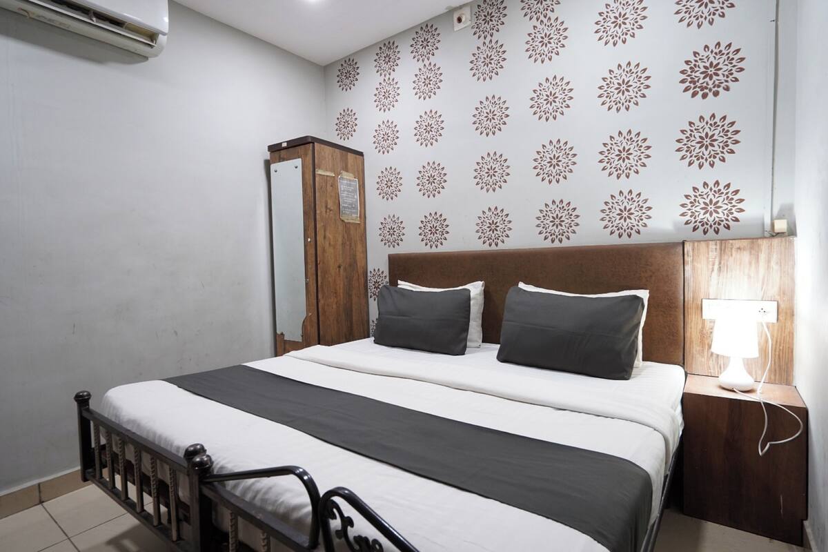 A bedroom with a bed, a wooden wardrobe, a nightstand with a lamp, and a wall with floral wallpaper.