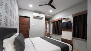 A bedroom with a bed, a ceiling fan, an air conditioning unit, a television, and a door. - Hotel Sai Inn (Ahmedabad)