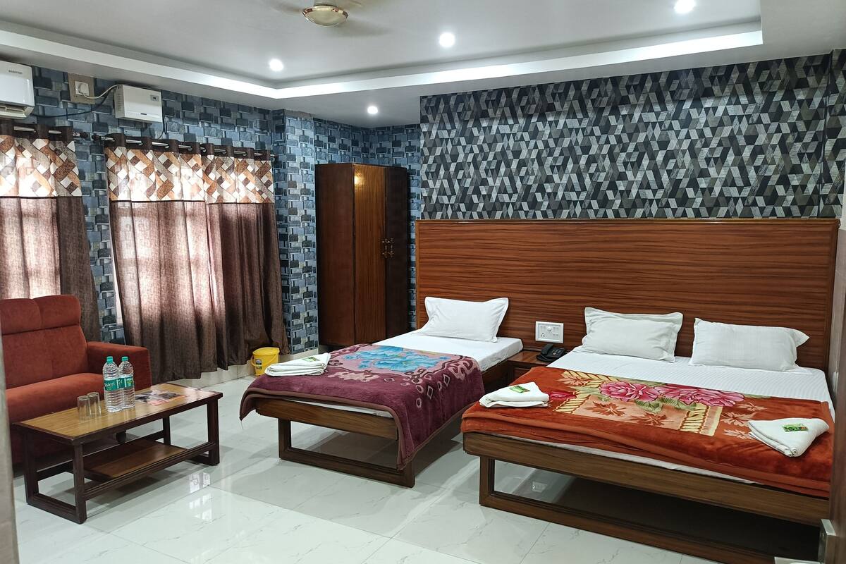 A hotel room with two beds, a sofa, a wooden table, and a wardrobe.