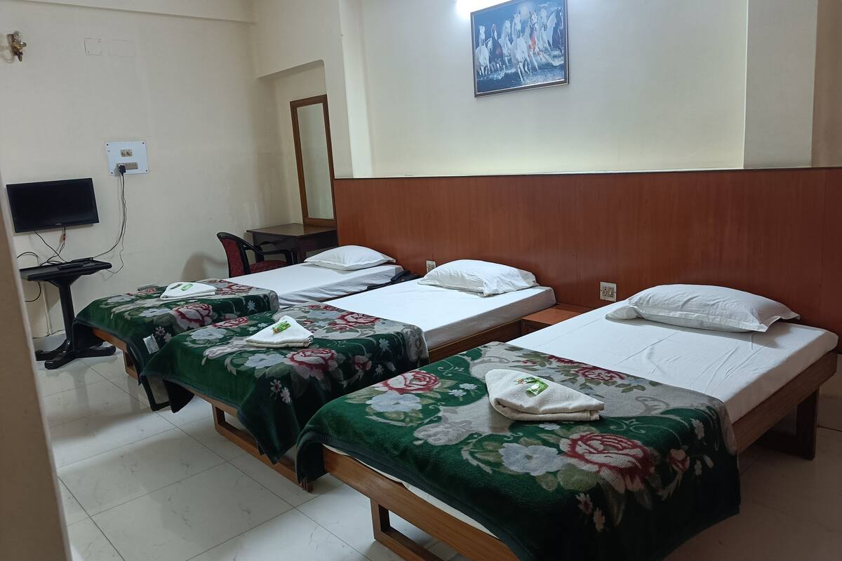 A hotel room with two single beds, a desk with a chair, a flat-screen TV mounted on the wall, and a painting above the beds.