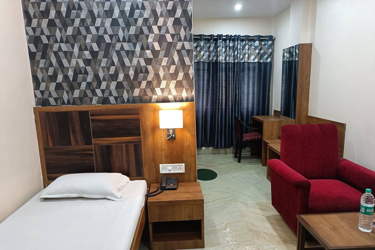 A hotel room with a bed, a desk, a chair, a nightstand, a lamp, a mirror, and a water bottle.