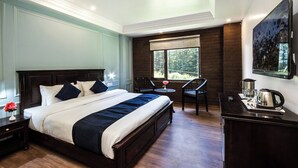 A bedroom with a large bed, a small table with chairs, a coffee maker, and a window with a view of trees. - Elysian Woods New Devidayar (Manali)