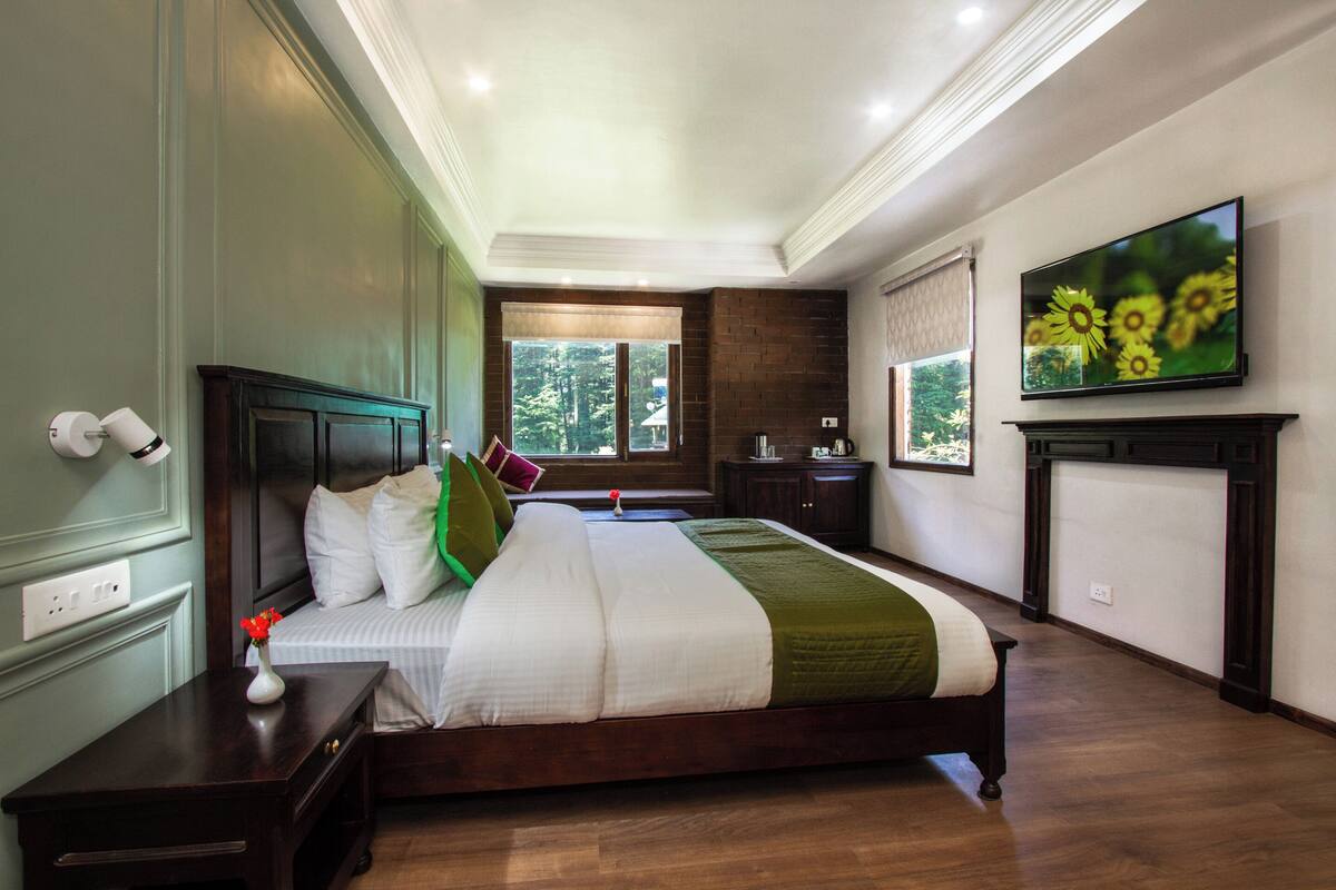 A bedroom with a large bed, a television mounted on the wall, and a window with a view of trees.
