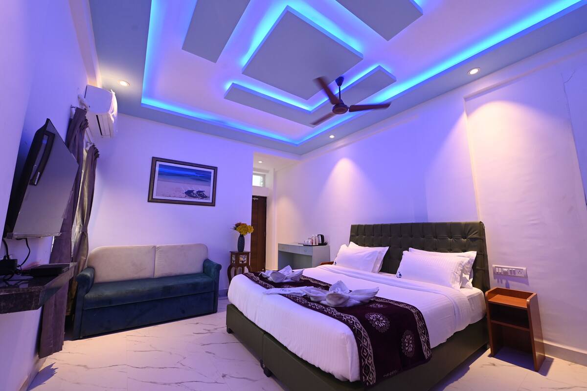 A modern hotel room with a bed, a sofa, a TV, and a ceiling fan.