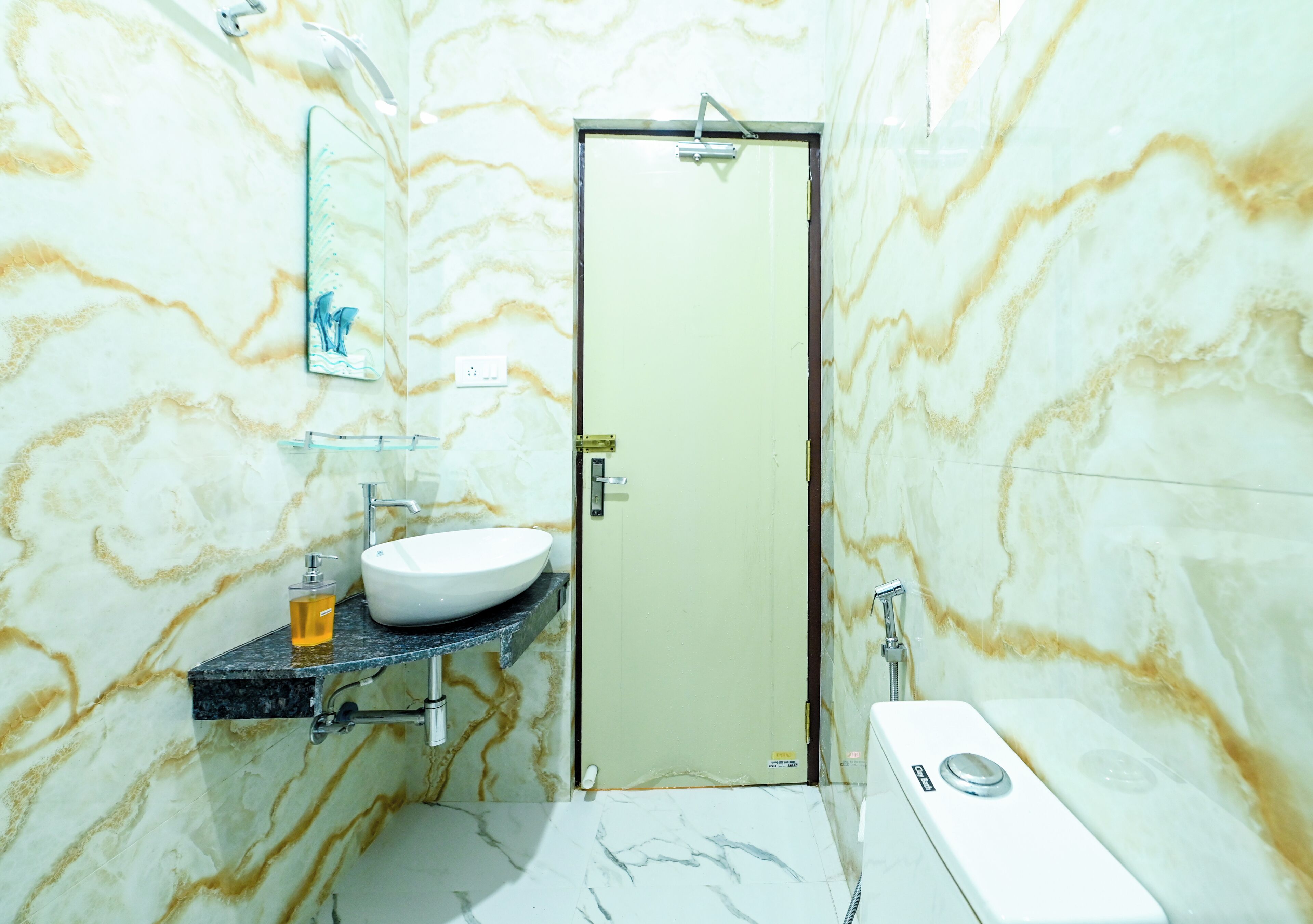 A bathroom with a marble wall, a white sink, a mirror, and a toilet.