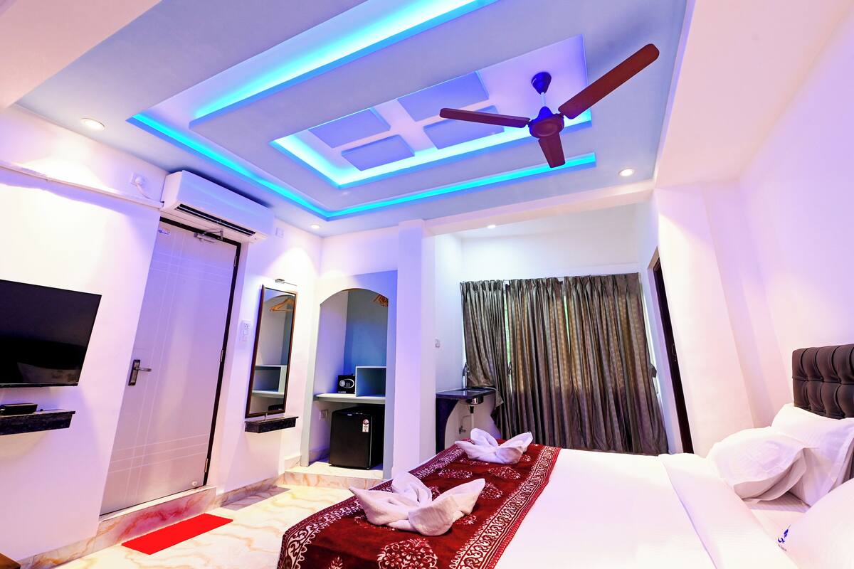 A modern hotel room with a bed, a ceiling fan, a TV, and a bathroom area.