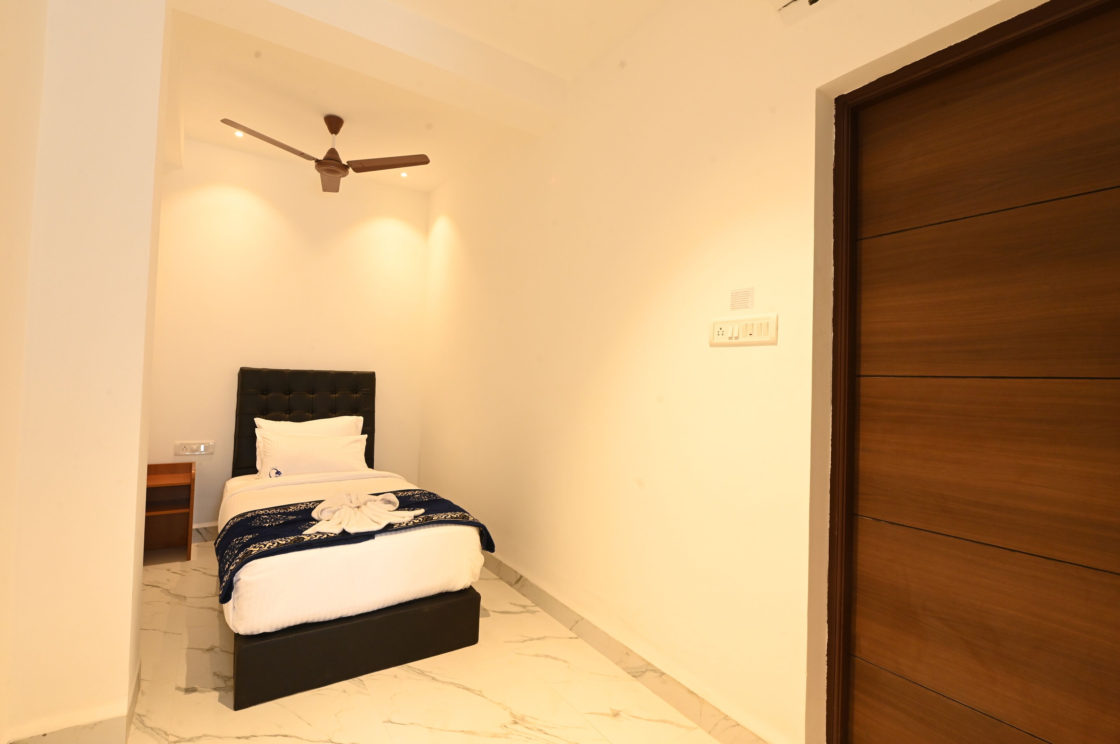 Camera da letto con un letto, una ventola a soffitto, una porta in legno e un comodino.