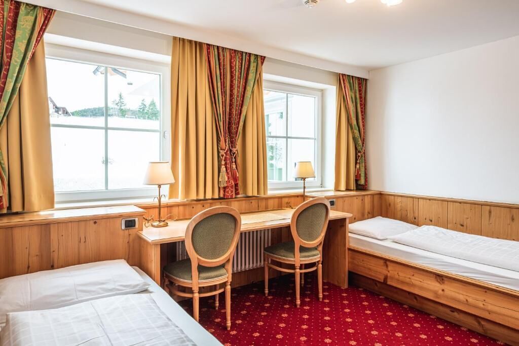Une chambre d’hôtel avec un bureau en bois, deux chaises, un lit et une fenêtre avec des rideaux.