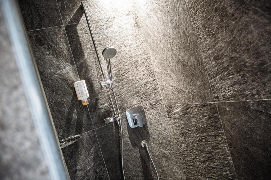 A shower area with a handheld showerhead and a wall-mounted faucet.