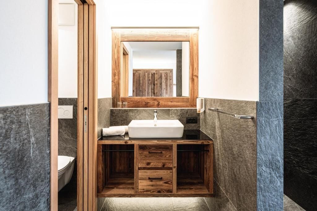 Un baño con tocador de madera, un lavabo blanco y un espejo encima.