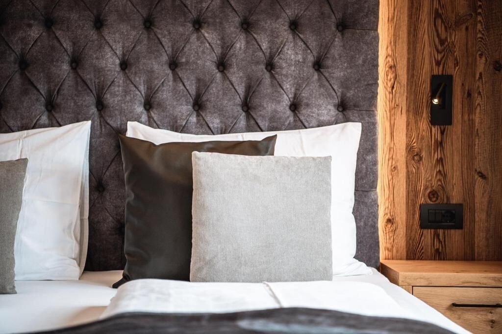 A bed with a tufted headboard, a wooden nightstand, and a wall-mounted light switch.