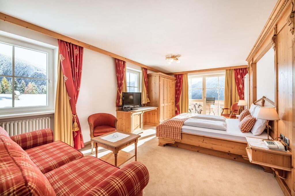 Een knus ingerichte kamer met een bed, bureau, televisie en een bank.
