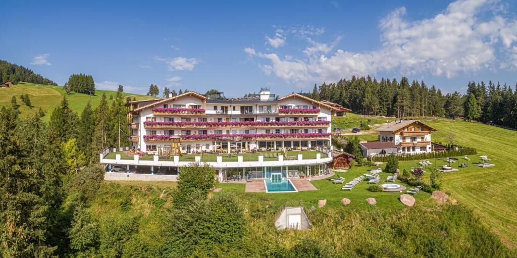 Ein mehrstöckiges Hotel mit Balkonen, einem Schwimmbecken und einer umliegenden Grünlandschaft.