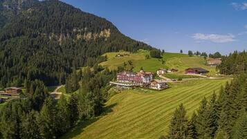 Un paisaje montañoso con un hotel que cuenta con varias edificaciones, un césped cuidado y una zona boscosa.