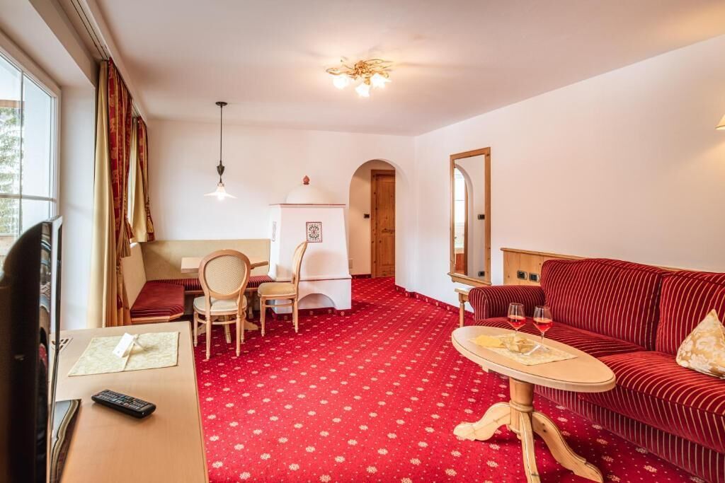 Una habitación de hotel con alfombra roja, un sofá, una mesa de comedor y un televisor.