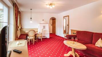 Una habitación de hotel con alfombra roja, un sofá, una mesa de comedor y un televisor.
