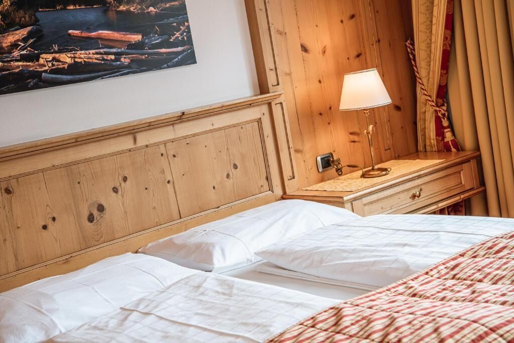 A hotel room with a wooden headboard, a bedside table with a lamp, and a bed with white linens.