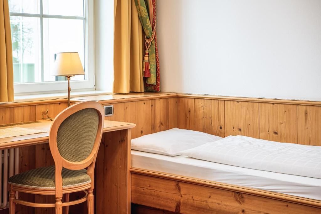 Ein Zimmer mit Holzboden, einem Einzelbett, einem Schreibtisch und einem Stuhl.