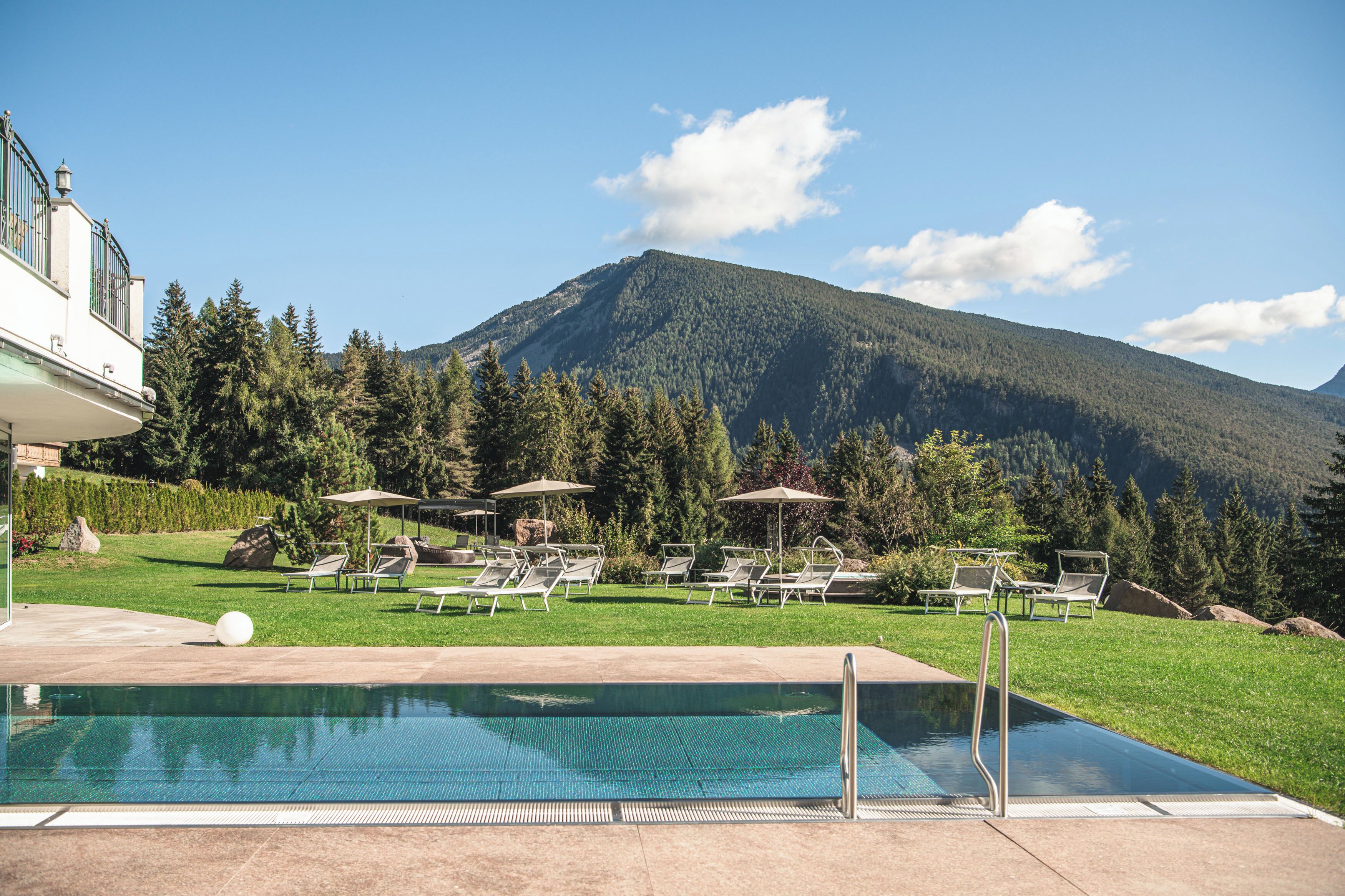 A pool area with lounge chairs and umbrellas, surrounded by a lush landscape and a mountain in the background.