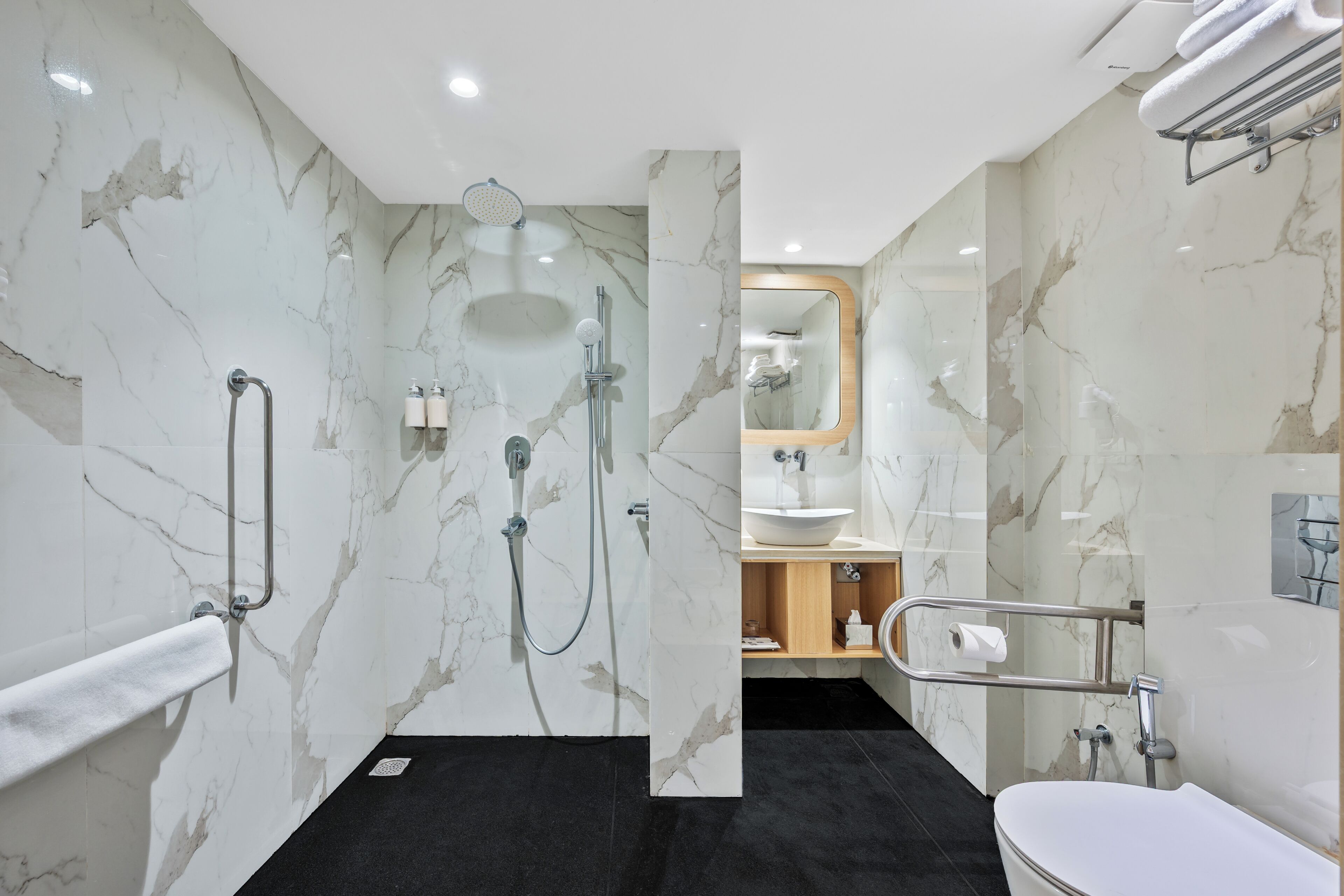 A modern bathroom with marble walls, a black floor, a white bathtub, and a shower area with grab bars.