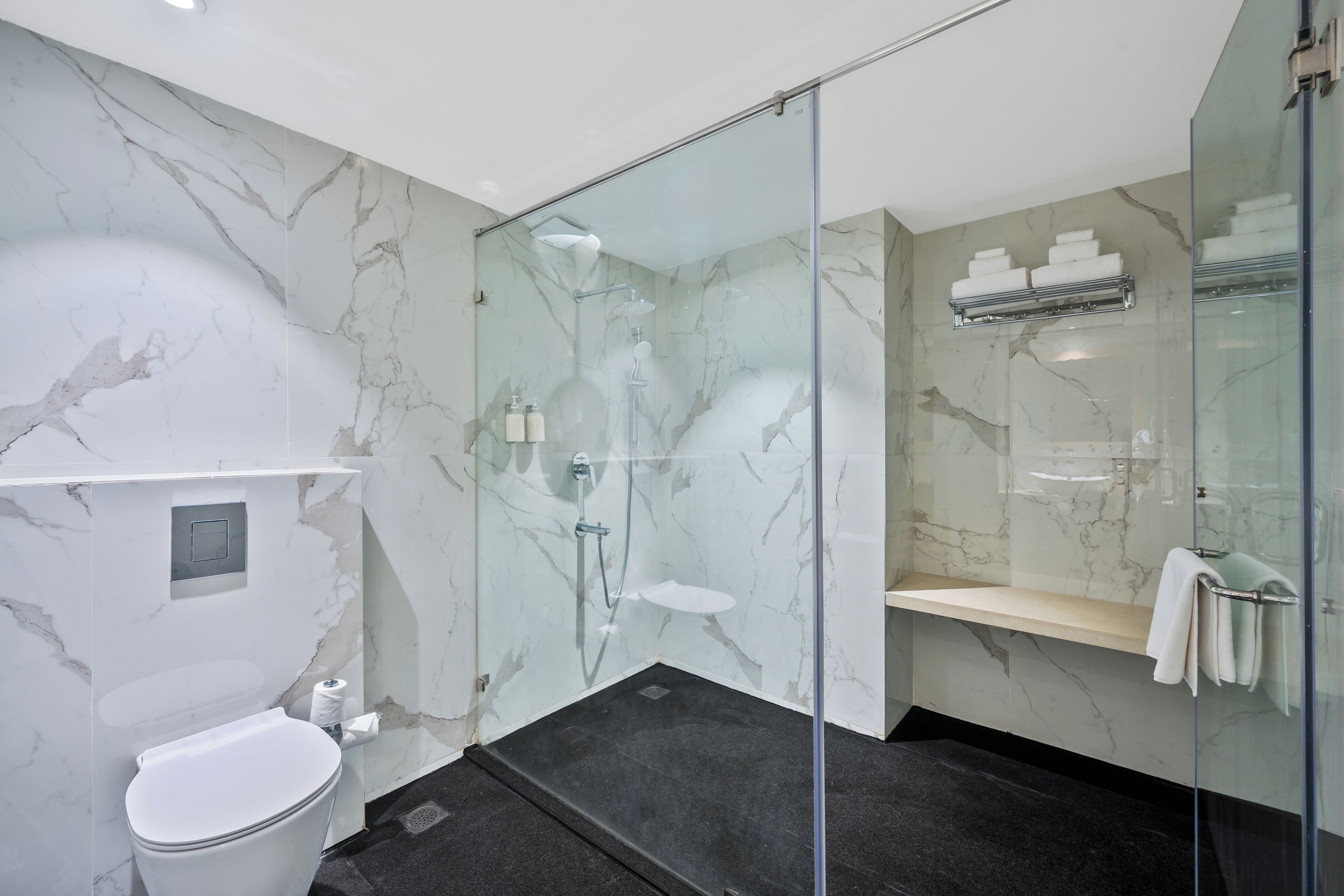 Une salle de bain moderne avec une douche à parois de verre, des murs en marbre, des toilettes blanches et un porte-serviettes avec des serviettes pliées.
