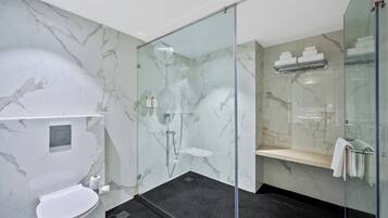 Un baño moderno con ducha envuelta en vidrio, pared de mármol, inodoro y estante con toallas.