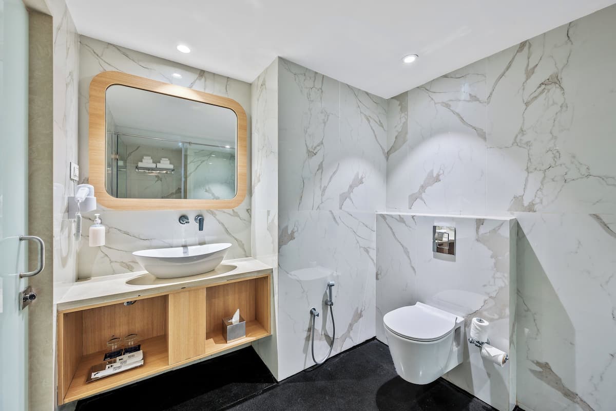 A modern bathroom with a marble sink, a wooden vanity, a large mirror, a toilet, and a shower.