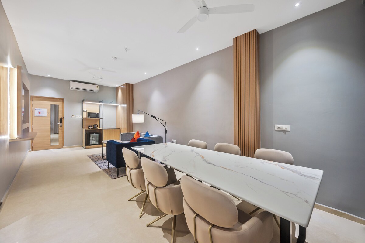 A modern conference room with a marble table, beige chairs, a ceiling fan, and a kitchenette in the background.