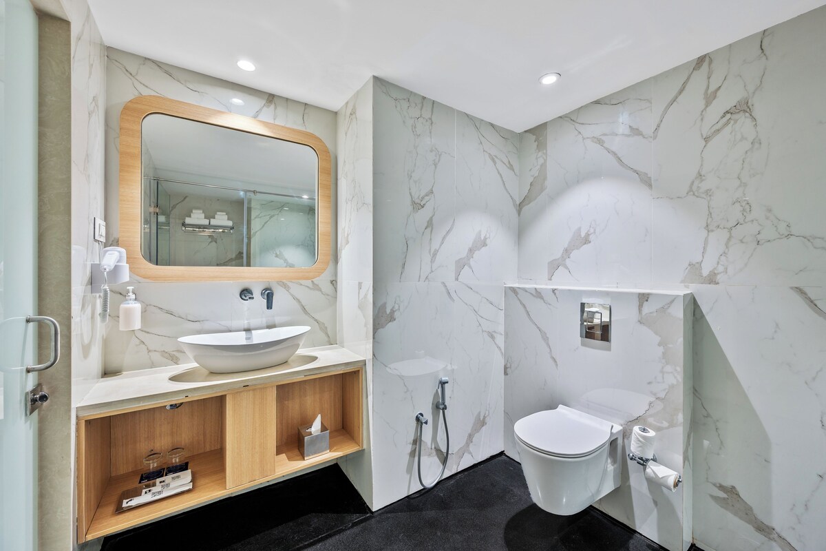A modern bathroom with a marble sink, a wooden vanity, a large mirror, a toilet, and a shower.
